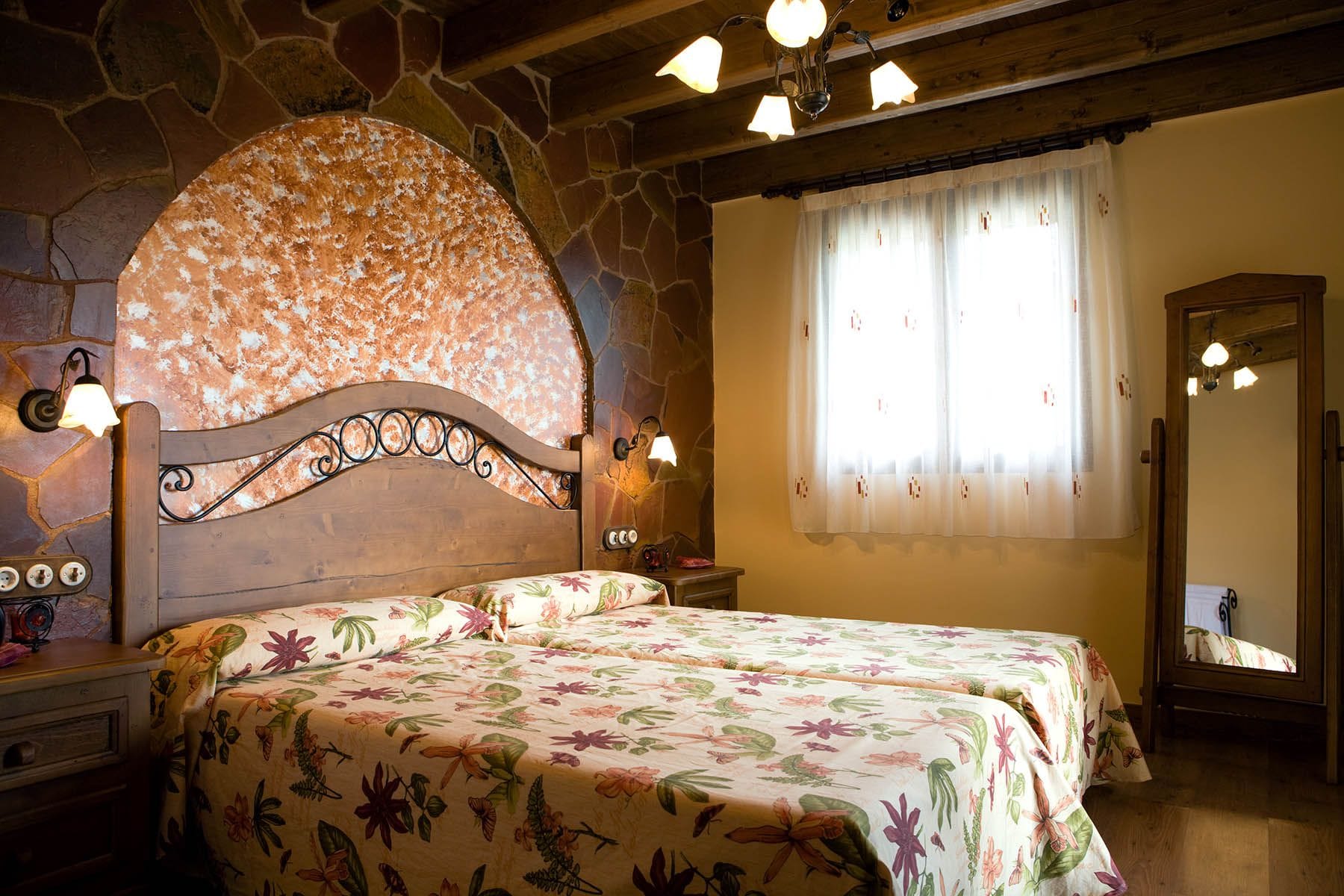Dormitorio con dos camas individuales, cabecero de madera y paredes de piedra de Mas d’Albalat