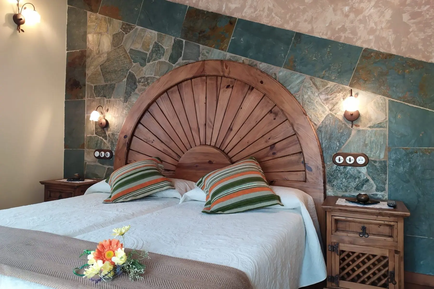 Dormitorio con cama de matrimonio, cabecero de madera y pared de piedra