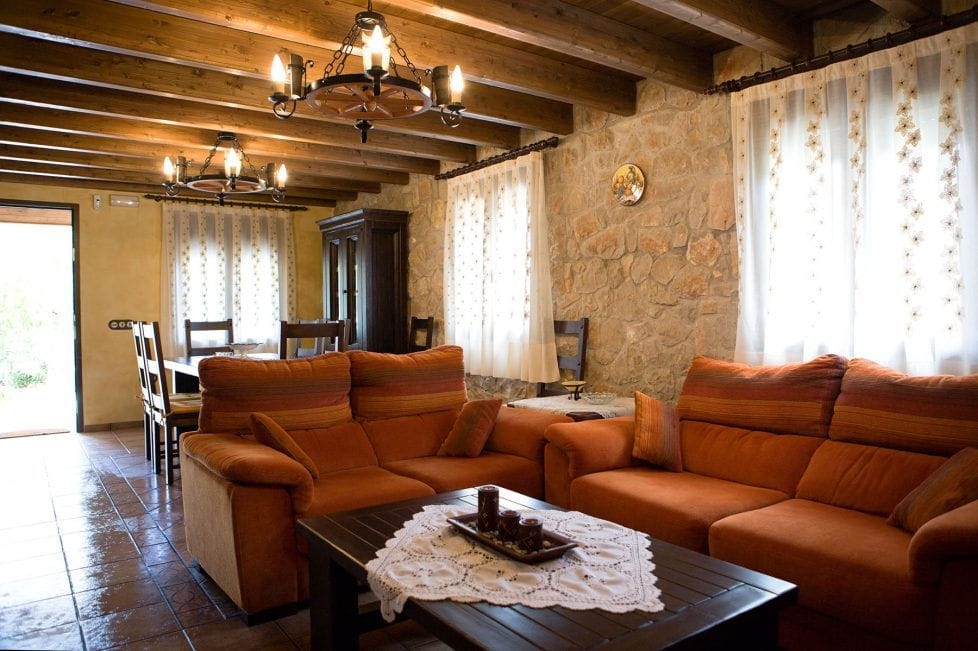 Salón de Mas d’Albalat con sofás, paredes de piedra y vigas de madera